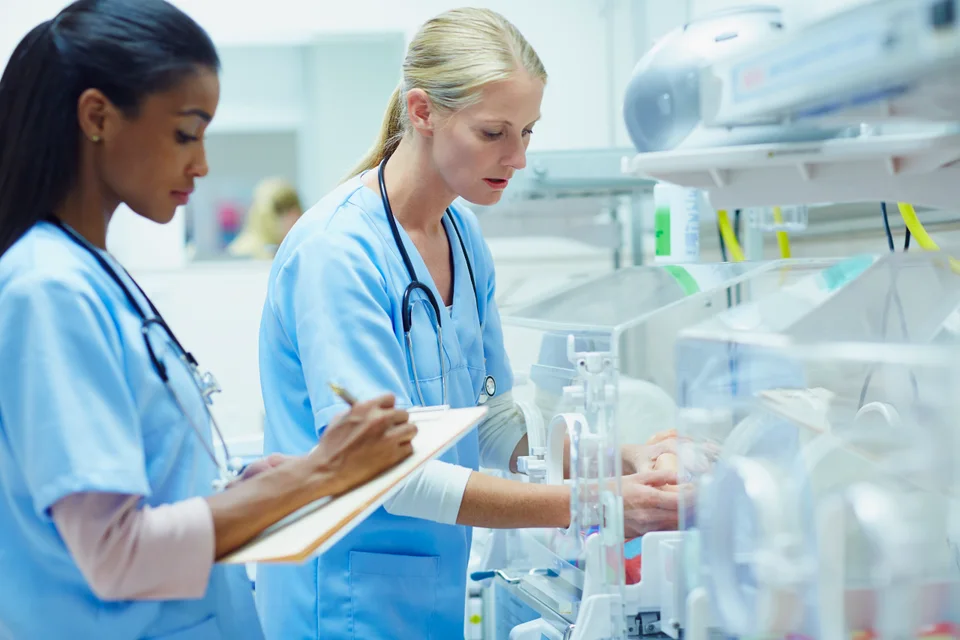 Two healthcare professionals caring for an infant in a neonatal unit